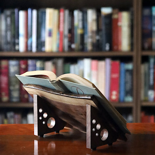Open book on a wooden stand with a bookshelf filled with books in the background